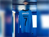 En lyseblå fodboldtrøje med lange ærmer, hvor der på ryggen står GREENTEL og THEMSEN 7, hængende på en krog i loftet.