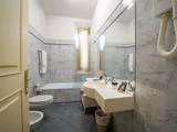Et moderne badeværelse med marmorvægge, et badekar med matteret glas, et bidet, et toilet, et stort spejl, to håndvaske og en væghængt hårtørrer.