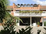 Hotellets ydre med Hotel Executive-skilt, murstensfacade, planter på balkonen og grønne områder i forgrunden under en blå himmel.