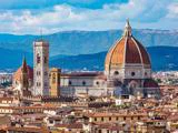 En panoramaudsigt over Firenze, der viser katedralen Santa Maria del Fiore med sin store røde kuppel og klokketårn mod en baggrund af bakker og blå himmel.