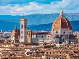 Udsigt over Firenzes katedral Santa Maria del Fiore med den store kuppel med røde fliser, klokketårnet og de omkringliggende historiske bybygninger på en baggrund af bjerge og blå himmel.