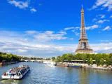 En sightseeingbåd sejler på Seinen i Paris, hvor Eiffeltårnet og de grønne træer er synlige under en lyseblå himmel.