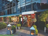Udendørsservering og indgang til Restaurant Under Klippen med grønne områder, glasvinduer og lanterner med levende lys på terrassen.
