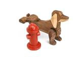 En hundefigur af træ står ved siden af en lille, rød legetøjsbrandhane på en hvid baggrund.