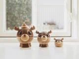 Tre rensdyrfigurer af træ i forskellige størrelser med store øjne og gevirer står i en hvid vindueskarm, hvor sollyset strømmer ind.
