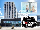 En moderne bygning i flere etager, et billede af to børn, der leger i en pool, og Baboon City-logoet med fede sorte og hvide bogstaver.