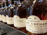 Nærbillede af flere flasker Fary Lochan dansk single malt whisky opstillet på en hylde med brune etiketter og ravfarvet væske indeni.