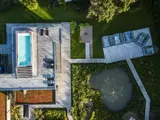 Luftfoto af et moderne hus med pool på taget, træterrasse, have og en dam med springvand omgivet af grønne områder.