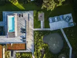 Luftfoto af et moderne hus med pool på taget, træterrasse, have, gangstier og en lille dam omgivet af grønt.