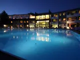En stor udendørs swimmingpool om natten med en moderne, veloplyst hotelbygning i baggrunden.
