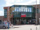 En person skubber en indkøbsvogn hen mod indgangen til et Fleggaard-supermarked med en glasfacade og butikkens logo over dørene.