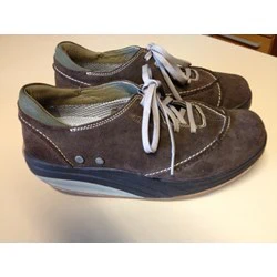 Et par brune ruskindssnøresko med tykke, buede såler og synlige hvide syninger, placeret på en lys overflade.