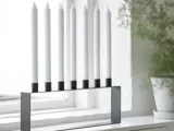 En moderne, minimalistisk menorah med syv utændte hvide lys står i vindueskarmen ved siden af en grøn potteplante.