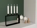 En moderne sort lysestage med fire tændte hvide lys står på en hvid flade ved siden af træpynt og to hvide stjernedekorationer på en grøn og hvid væg.