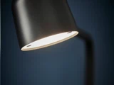 Nærbillede af en moderne sort skrivebordslampe, der er tændt og kaster et blødt hvidt lys mod en mørkeblå baggrund.