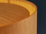 Nærbillede af en glat, buet træoverflade med varm belysning, der fremhæver træets årer og afrundede kanter mod en mørk baggrund.