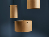 Tre cylindriske pendler i træ hænger op ad en mørkeblå væg, kaster bløde skygger og skaber en moderne, minimalistisk æstetik.