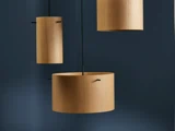 Tre cylindriske pendler i træ hænger op ad en mørkeblå væg, kaster bløde skygger og skaber en moderne, minimalistisk æstetik.