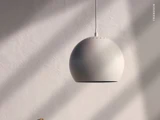 En moderne, kugleformet hvid pendel hænger ned fra loftet foran en lys, struktureret væg og kaster bløde skygger. Ordet FRANDSEN står lodret på højre side.