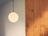 En rund, hvid pendel hænger ned fra loftet ved siden af en trævæg med et glat, naturligt åringsmønster.