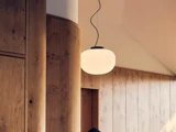 En rund, hvid pendel hænger fra loftet i et rum med lyse træpaneler på væggene og buede trædetaljer.
