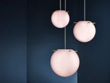 Tre lyserøde, runde pendler med gulddetaljer hænger op ad en mørkeblå væg og skaber et moderne og elegant indretningslook.