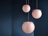 Tre runde, blanke pink pendler hænger i forskellige højder mod en mørkeblå væg og skaber et moderne og elegant look.