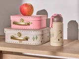 Et rødt æble ligger på to stablede dekorative kufferter, en lyserød og en beige med træmønstre, ved siden af en beige vandflaske på en træhylde.