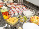 En buffet med udskåret frugt, cherrytomater, peberfrugt i skiver, skåle med yoghurt, halve kiwier og stablede yoghurtbægre på en disk.