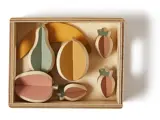 Legetøjsfrugtsæt af træ i en rektangulær æske med stykker formet som en banan, pære, appelsin, æble og to jordbær i dæmpede pastelfarver.