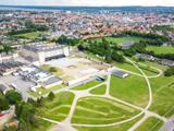 Luftfoto af en by med en stor historisk bygning, grønne parkområder, stier og omkringliggende boligkvarterer.