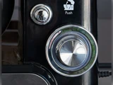 Nærbillede af en metallisk drejeskive med tallene 1 til 4 og en trykknap over den på et sort køkkenapparat. En refleksion er synlig på urskivens overflade.