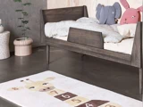 Børneværelse med en træseng, dyreformede puder og et tæppe med et hopscotch-design med en girafillustration.