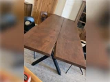 Et spisebord i træ med en naturlig deling på midten, sat på sorte metalben, omgivet af sorte stole i et moderne rum.