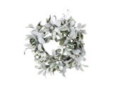 En rund krans af frostede grønne blade og små hvide bær, arrangeret i et cirkulært mønster mod en hvid baggrund.