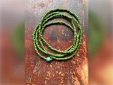 En lang streng af små grønne perler med en større perle er rullet op på en rustik, rødbrun træoverflade.