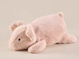 En blød, lyserød plysgris ligger på maven mod en almindelig beige baggrund.