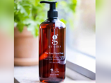 En brun pumpeflaske med Grums The Kind Hand Soap i en vindueskarm med grønne planter i baggrunden.