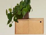 En bladgrøn potteplante står oven på en lille træhylde med to skydedøre op ad en almindelig lys væg.