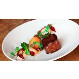 En gourmetret med et stegt stykke kød, en rund kroket, kunstfærdigt arrangerede grøntsager og mikrogrønt på en hvid tallerken på et træbord.