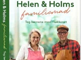 Forsiden af kogebogen Helen & Holms familiemad viser to voksne og to børn, der smiler i et køkken.