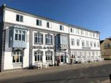 En hvid treetagers bygning med karnapper, mærket Hotel du Nord, med udeservering og danske flag under en klar blå himmel.