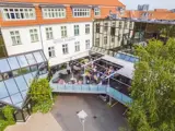 Luftfoto af mennesker, der spiser på en glasoverdækket terrasse på Hotel Europa, en hvid bygning med orange tagsten og store vinduer.