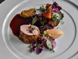 En gourmetret med kød i skiver, cremede puréer, grønt, spiselige blomster og en mørk sauce, kunstfærdigt anrettet på en hvid tallerken.