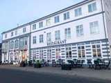 En hvid treetagers bygning med RESTAURANT- og HOTEL NORD-skilte, udeservering, potteplanter og danske flag ved indgangen.