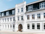 Hvid bygning i historisk stil med symmetriske vinduer, en central indgangsbue og et skilt med teksten Hotel Lidenlund over døren. Eksteriøret fremstår velholdt og indbydende.