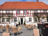 Udendørsservering foran en traditionel bygning med røde tagsten, danske flag, klippede træer og skilte med teksten "Hotel Ringkjøbing".