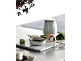 En sushirulle, tangsalat, wasabi, en skål med sojasauce, spisepinde og en keramisk kop er anbragt på en rektangulær bakke på et minimalistisk bord.