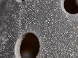 Nærbillede af en grå overflade med grov, kornet tekstur og flere cirkulære huller.