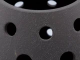 Nærbillede af et struktureret, mørkegråt objekt med runde huller og en ru, plettet overflade. Hvidt lys er synligt gennem hullerne i baggrunden.